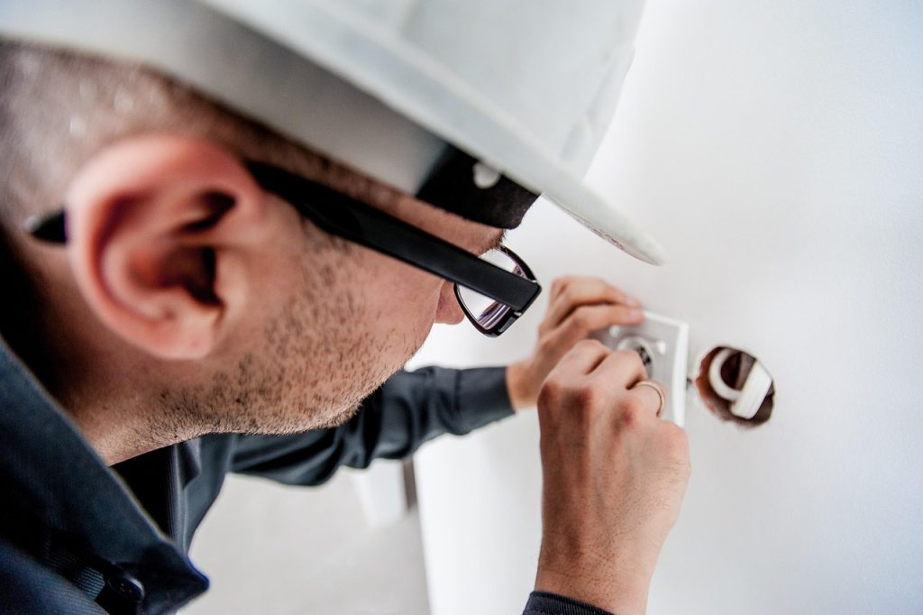 An electrician with a hard hat on fixing an electrical outlet